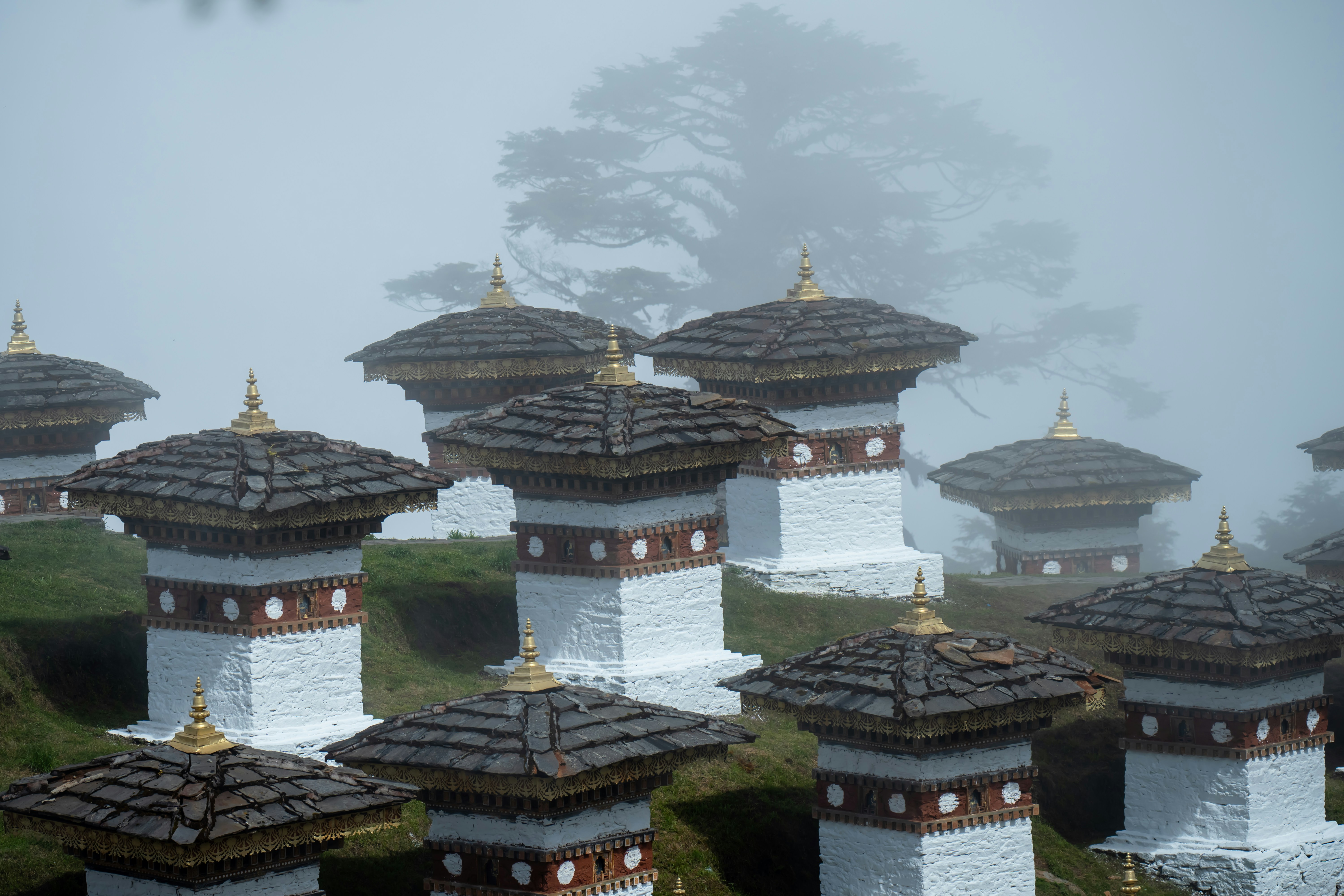 white and brown temple under white sky during daytime, 108 Memorial Chortens of Dochula Pass in Thimphu, Bhutan. Dochula Pass with Himalaya in background - Bhutan. In this pass, 108 memorial chortens or stupas known as Druk Wangyal Chortens have been built by Ashi Dorji Wangmo Wangchuk