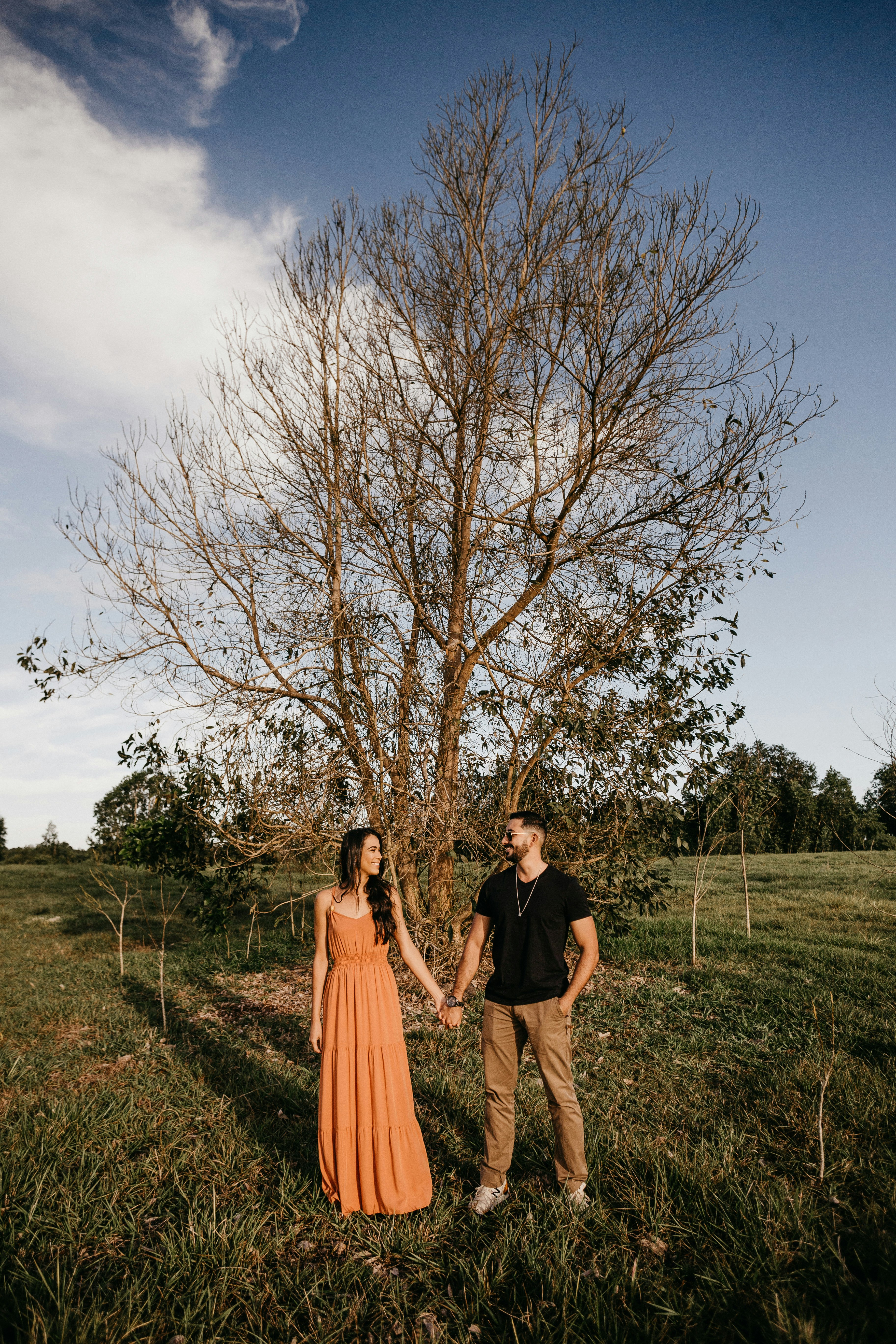 man and woman standing on green grass field near bare trees during daytime