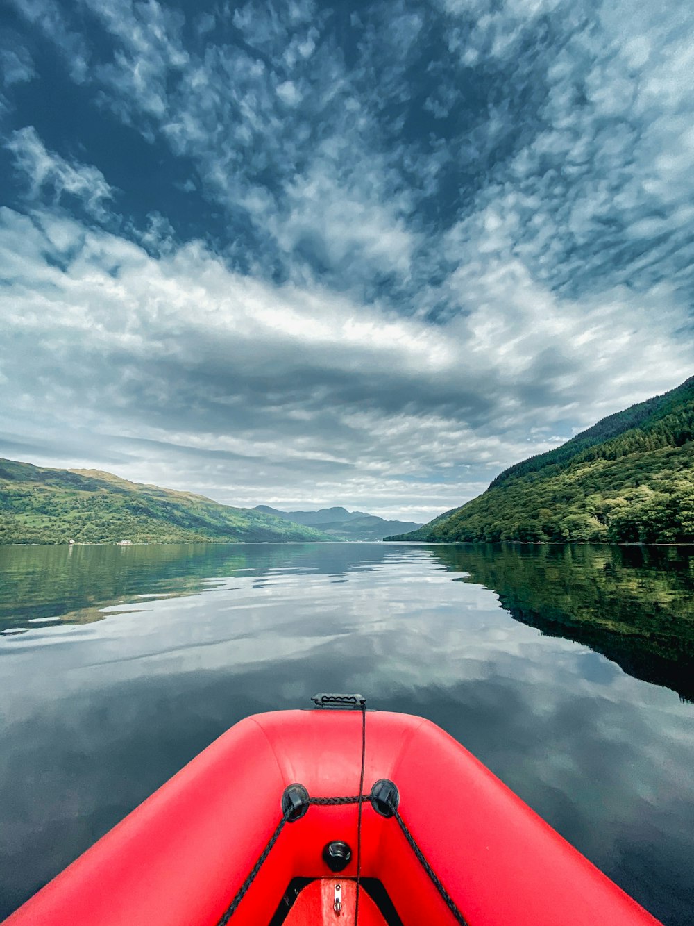 red kayak on lake near green mountains under white clouds and blue sky during daytime