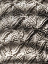 Intricate macrame pattern showcasing a series of interconnected diamond shapes, each formed by tightly knotted and looped threads. The texture is richly detailed, with depth created by the overlapping threads casting subtle shadows.