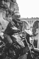 Close-up of a biker’s helmet and gloves resting on a rugged bike seat, with a scenic valley in the background