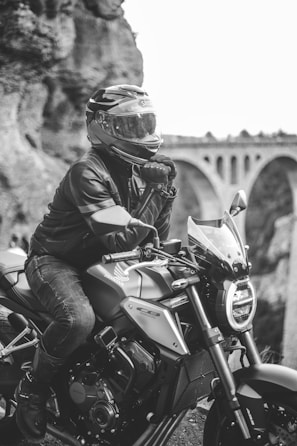 Close-up of a biker’s helmet and gloves resting on a rugged bike seat, with a scenic valley in the background