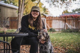 A smiling pet sitter gently petting a dog in a sunny backyard.