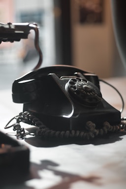 A vintage rotary phone resting on a wooden desk with a soft warm light highlighting its classic design.