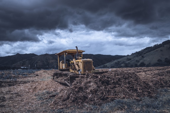 A rugged bulldozer pushing earth on a sunny day with a backdrop of open farmland.
