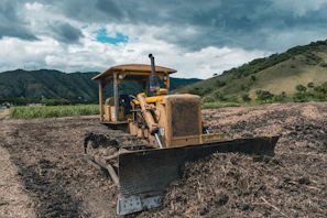 yellow and black heavy equipment on brown field under white clouds and blue sky during daytime