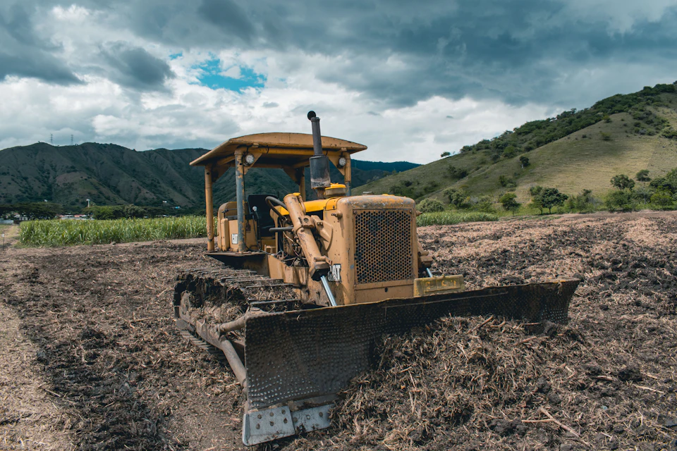 Bulldozer clearing and leveling a plot of land, with green hills behind
