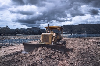 yellow and black heavy equipment on brown soil under cloudy sky during daytime
