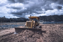 yellow and black heavy equipment on brown soil under cloudy sky during daytime