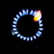 A stove burner with a ring of blue flames surrounding a central black disc, with a hint of orange flame visible at one spot.