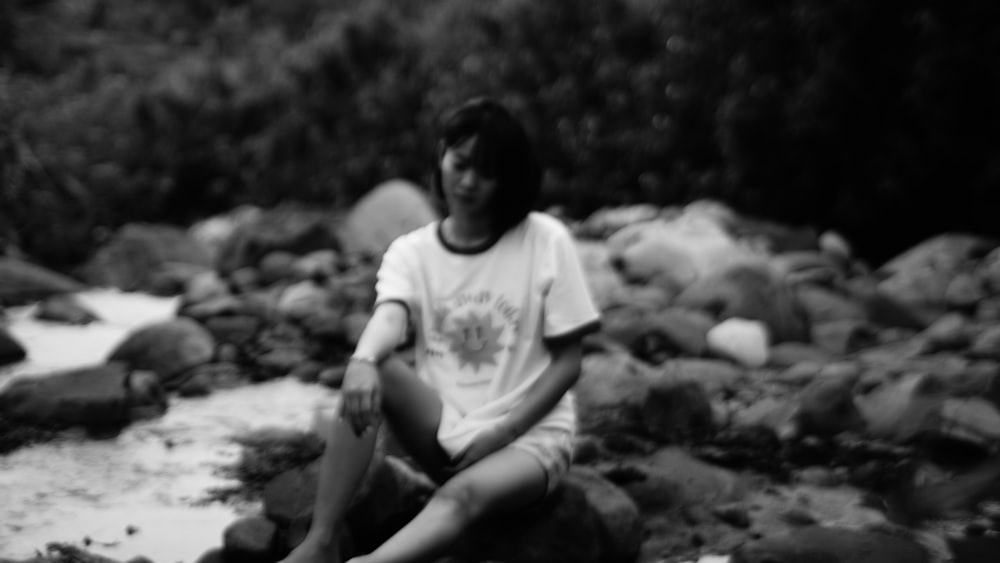 grayscale photo of boy sitting on rock