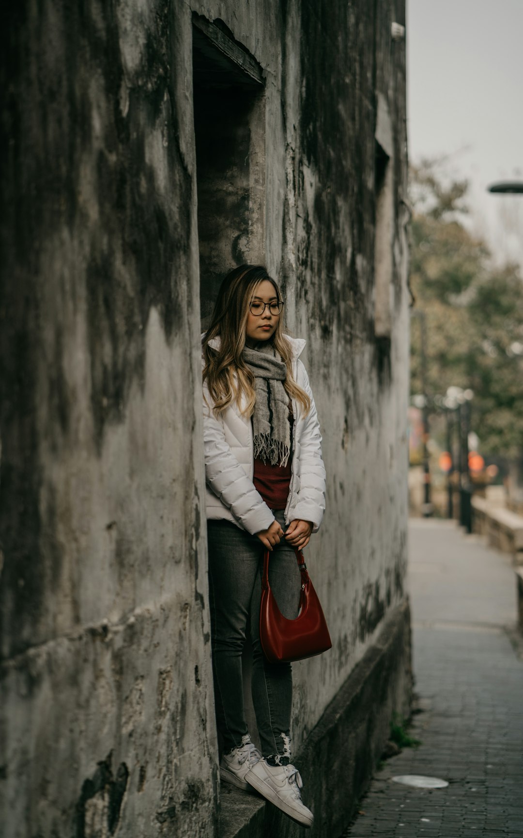 woman in white long sleeve shirt and red skirt leaning on gray wall