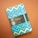 A notebook with a vibrant geometric design featuring zigzag patterns in shades of blue and gold. The cover has a black label with gold lettering that reads 'Castelli Milano Oro Collection'. A matching blue elastic band encircles the notebook, set against a muted brown background.