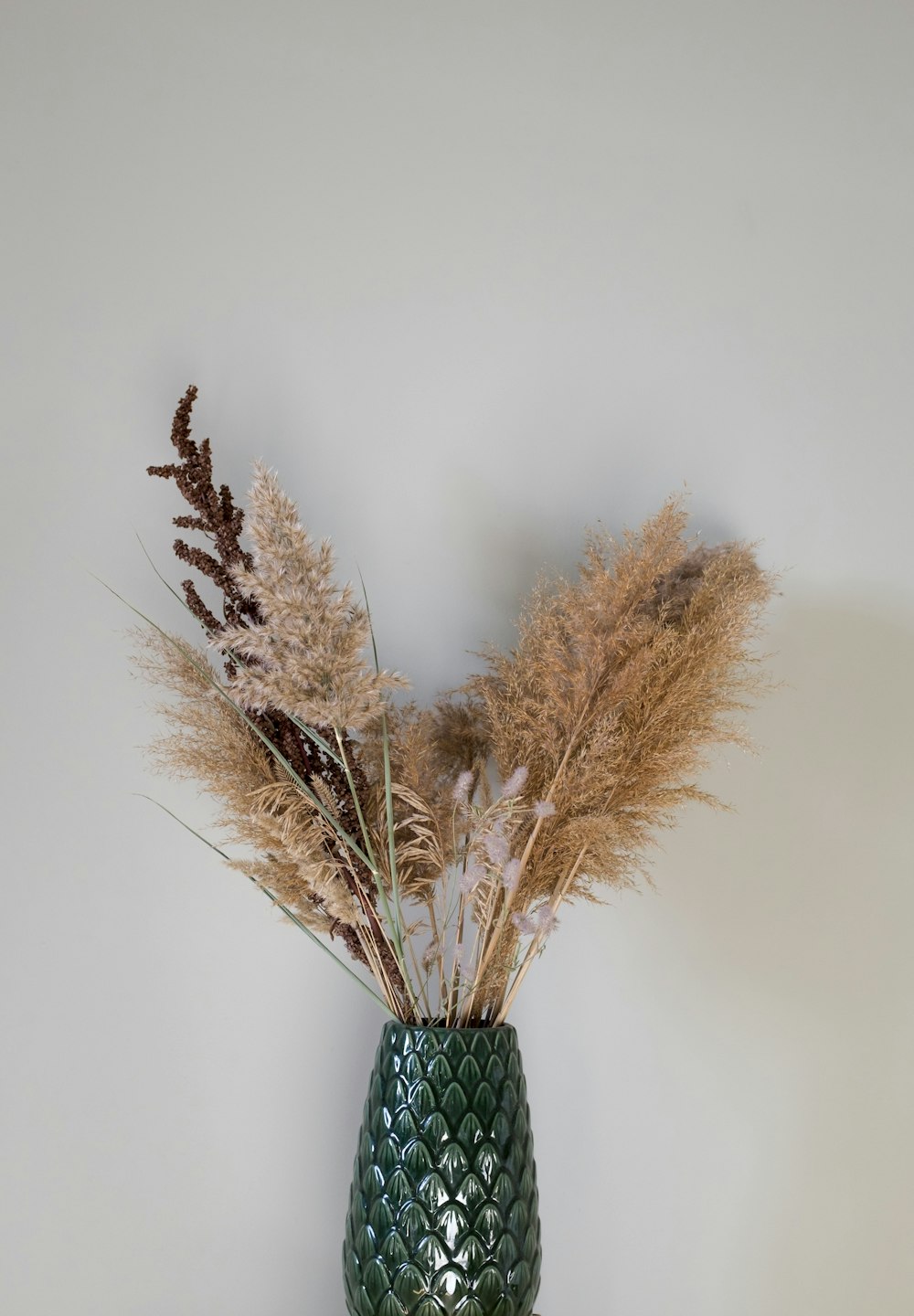a green vase with dried plants in it