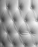 A detailed image of tufted upholstery with a diamond pattern and buttons securing the fabric at regular intervals. The texture of the material is clearly visible, with a soft sheen indicating high-quality leather or a similar material.