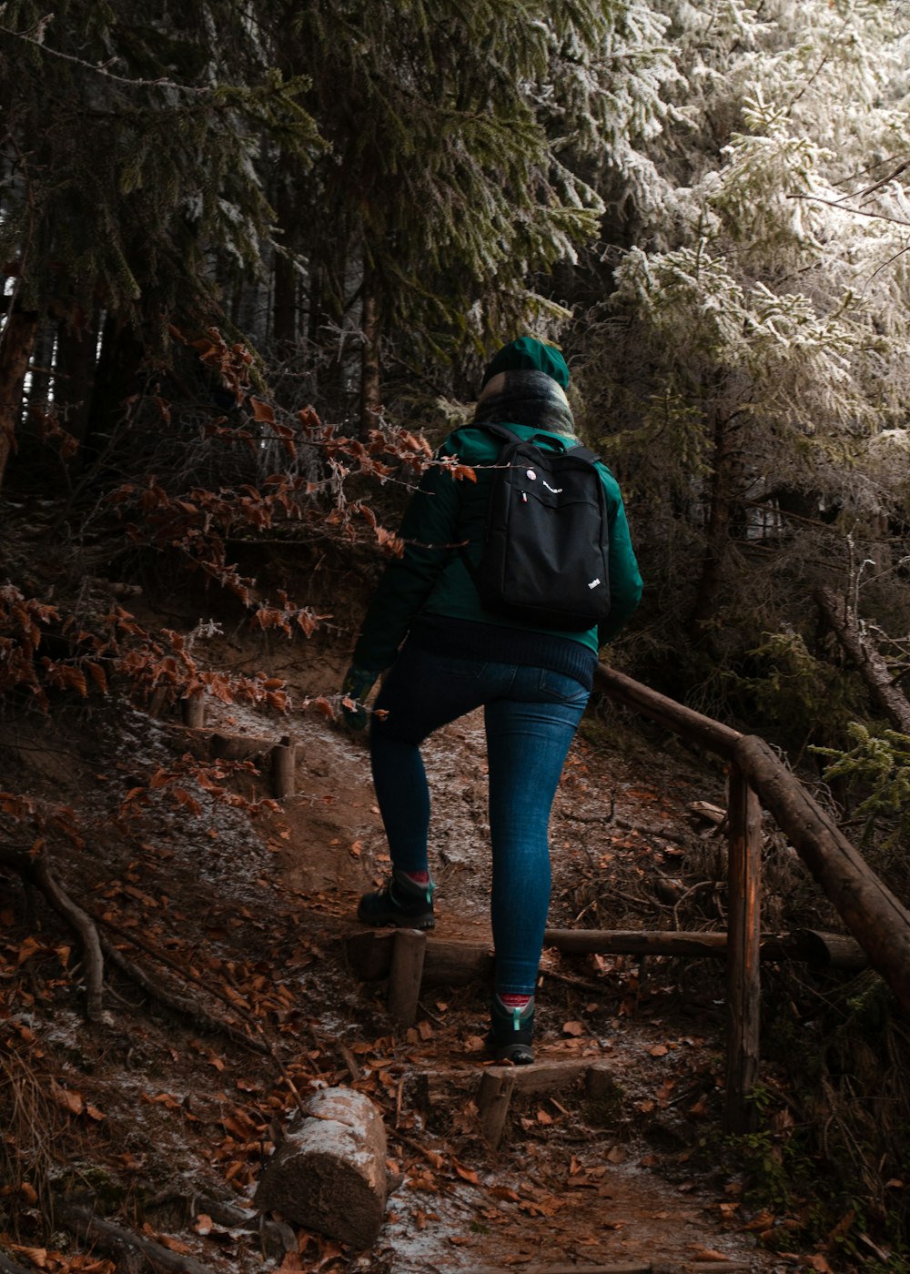 woman in blue denim jeans and black jacket standing on brown wooden bridge during daytime