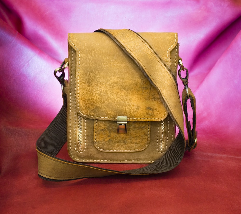 brown leather sling bag on pink textile