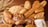 A basket filled with a variety of freshly baked bread, including baguettes, round loaves, and rolls. The bread features different textures and crust patterns, with some topped with seeds. To the left, wheat stalks add an organic touch to the arrangement.