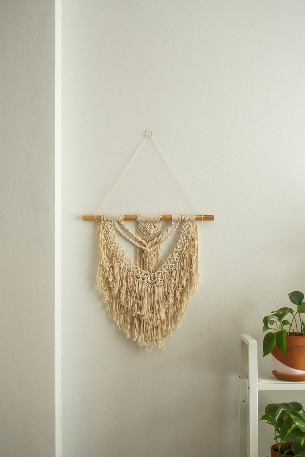 a wall hanging on a white wall next to a potted plant