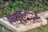 Granola bars covered with chocolate sit on a wooden cutting board. They are placed outdoors on green grass, and the bars have a texture of oats and other grains mixed with the chocolate.
