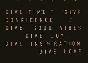 A series of motivational phrases are displayed in neon-style text against a dark background. The phrases include 'give time', 'give confidence', 'give good vibes', 'give joy', 'give inspiration', and 'give love'. The words are arranged in a structured, grid-like format, creating a visually impactful and positive message.