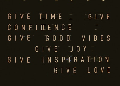 A series of motivational phrases are displayed in neon-style text against a dark background. The phrases include 'give time', 'give confidence', 'give good vibes', 'give joy', 'give inspiration', and 'give love'. The words are arranged in a structured, grid-like format, creating a visually impactful and positive message.