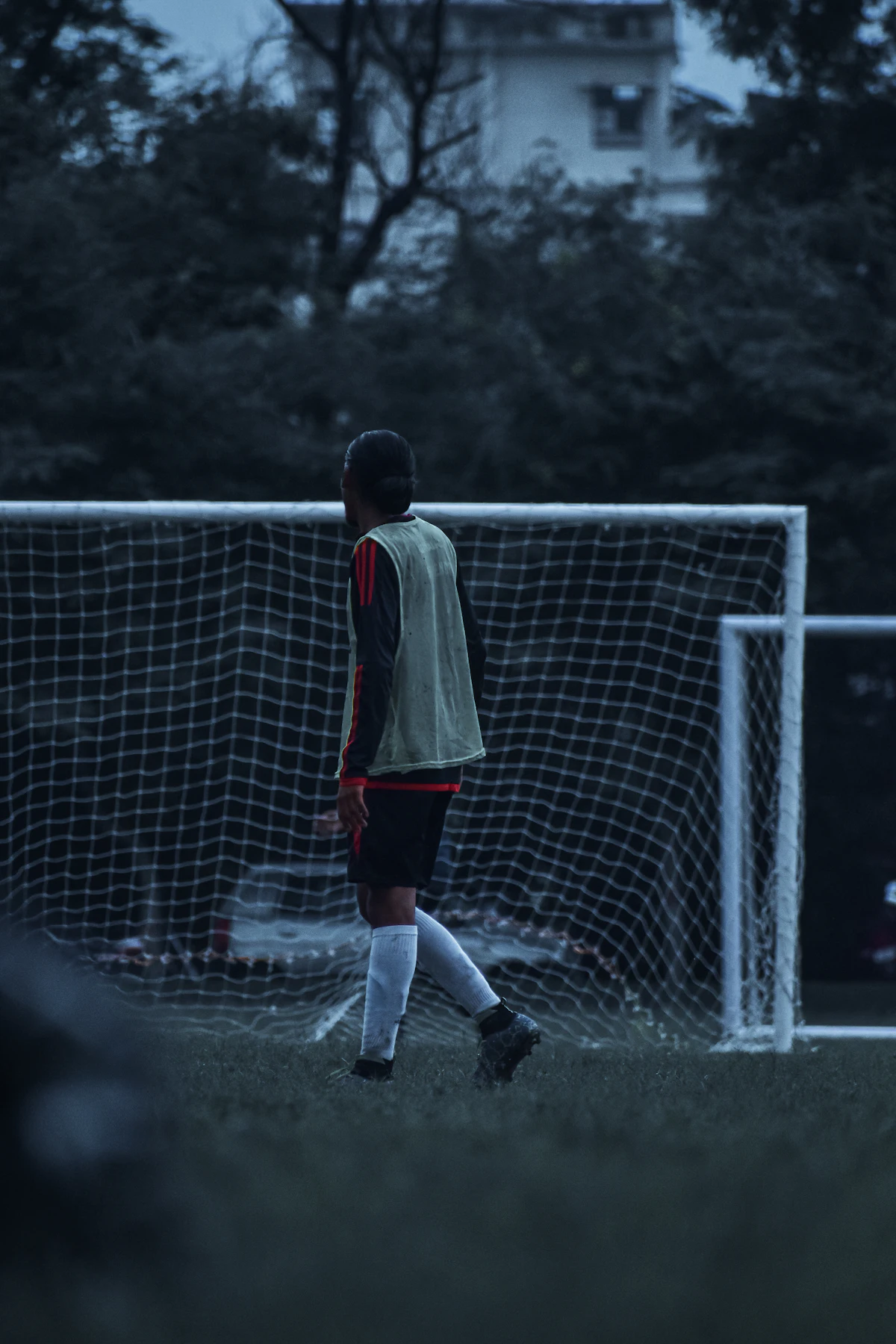 A player in a training bib waits by the goal at dusk
