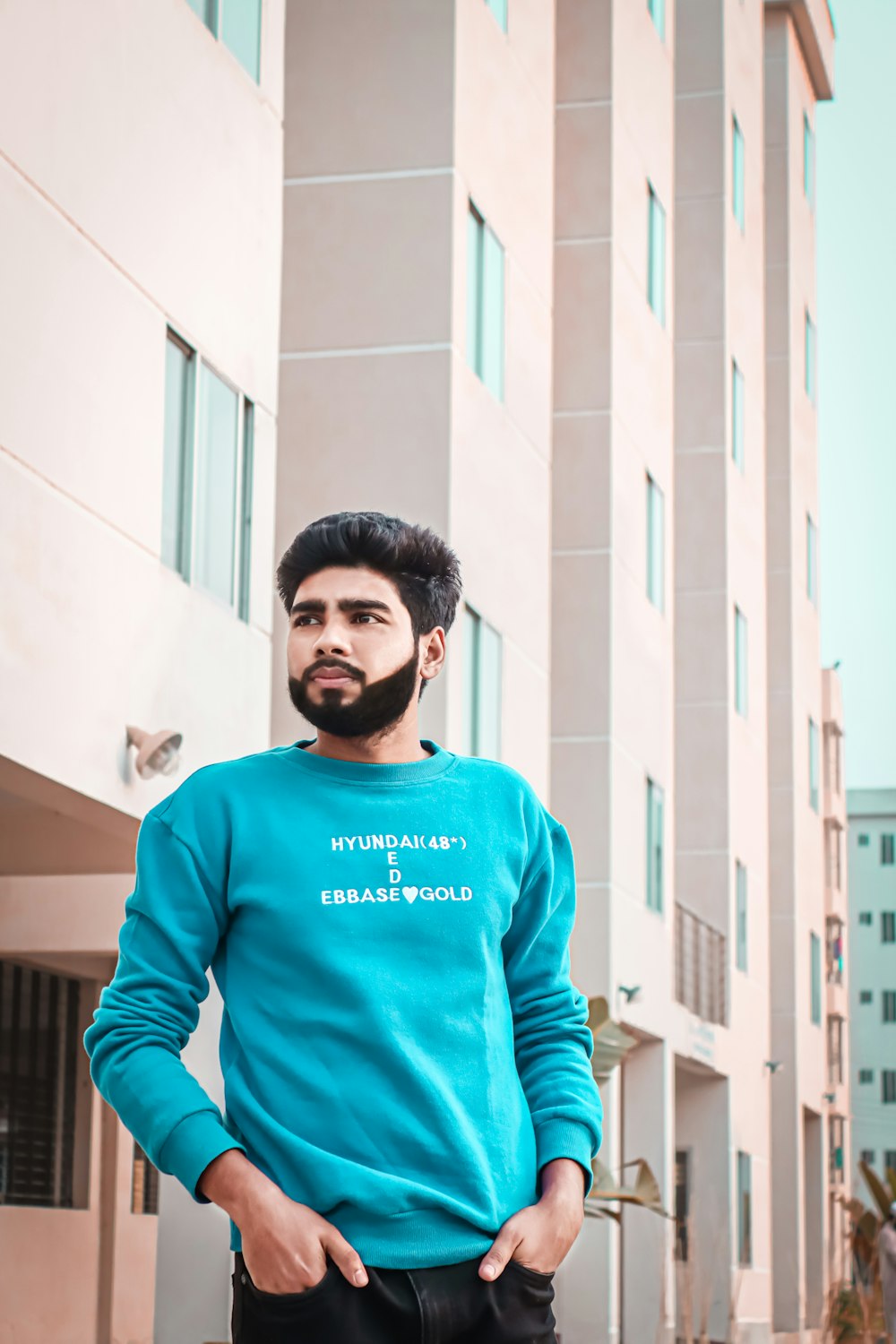 man in blue crew neck long sleeve shirt standing near white concrete building during daytime