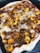 A close-up view of a homemade pizza topped with various ingredients such as fried cauliflower, spices, and bits of herbs on a thin crust. The edges appear slightly crisped, and the toppings are evenly spread across the surface, giving it a hearty and rustic appearance.