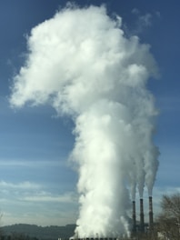 Smoke stacks rising from a thermal power plant against a clear blue sky with workers conducting safety checks.