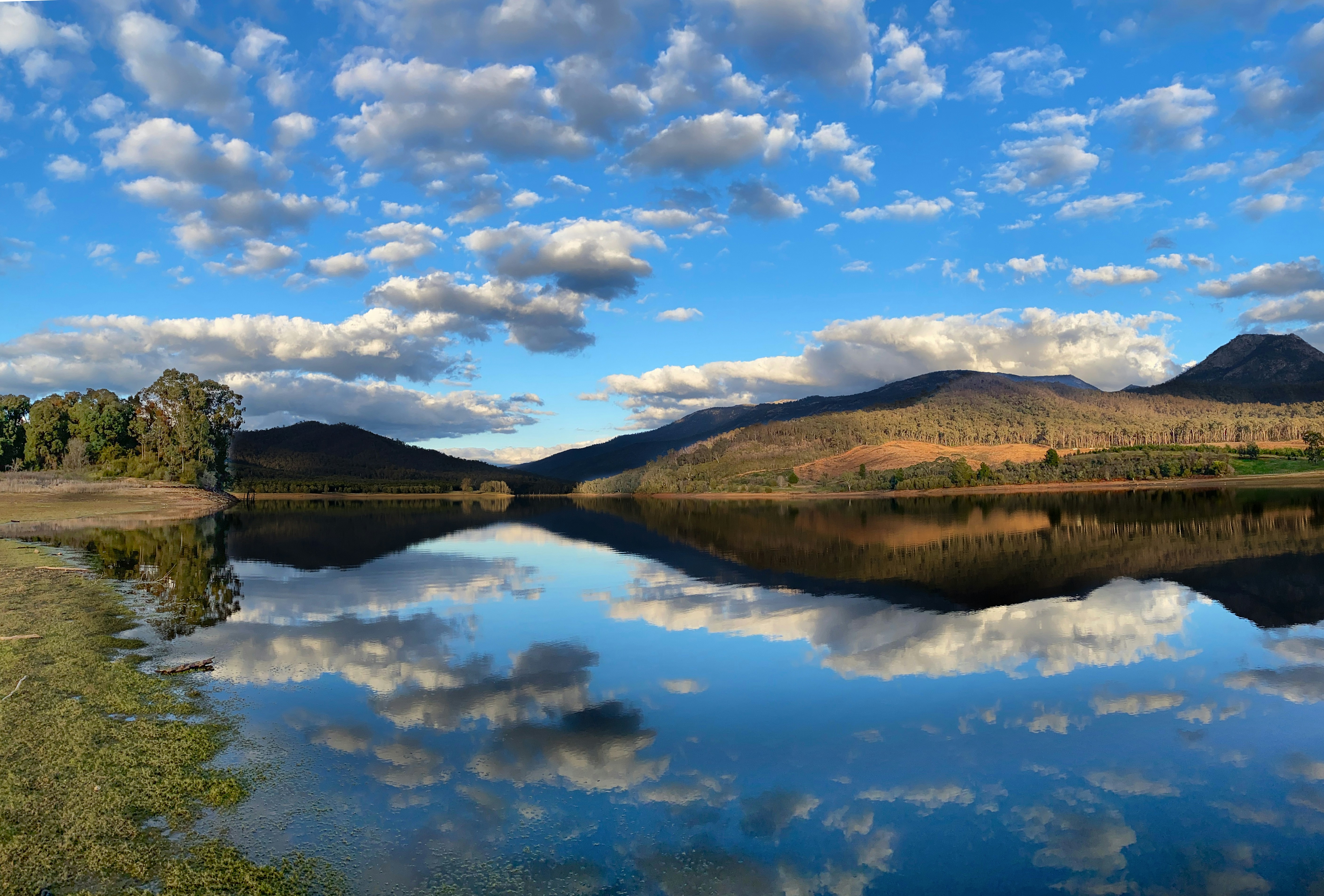 green and brown mountain beside lake under blue sky and white clouds during daytime