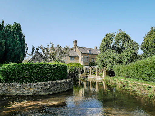 Cozy riverside cottage nestled among lush greenery under a clear blue sky.