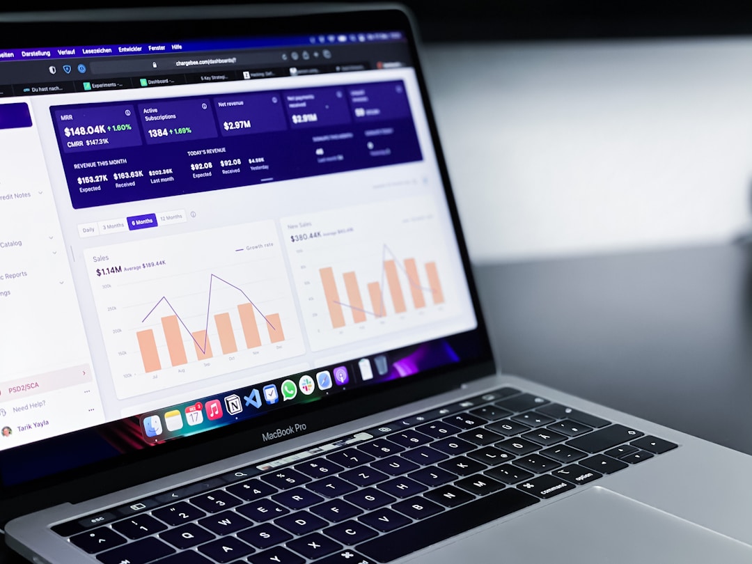 Laptop screen with a financial dashboard showing active subscriptions, revenue metrics, and performance graphs, placed on a dark desk.