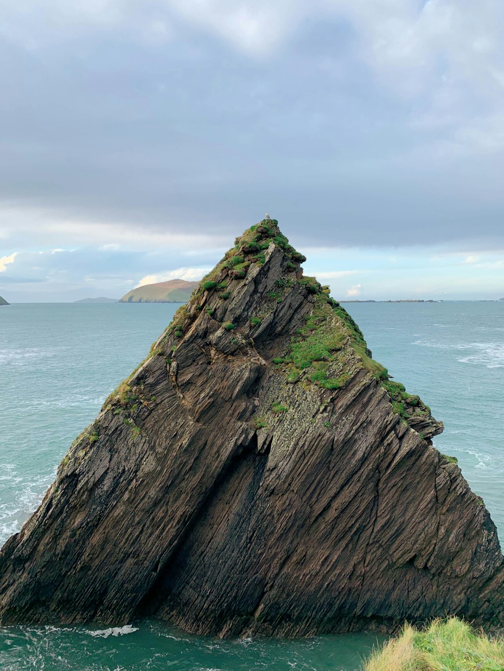 brown and green mountain beside sea under white clouds during daytime