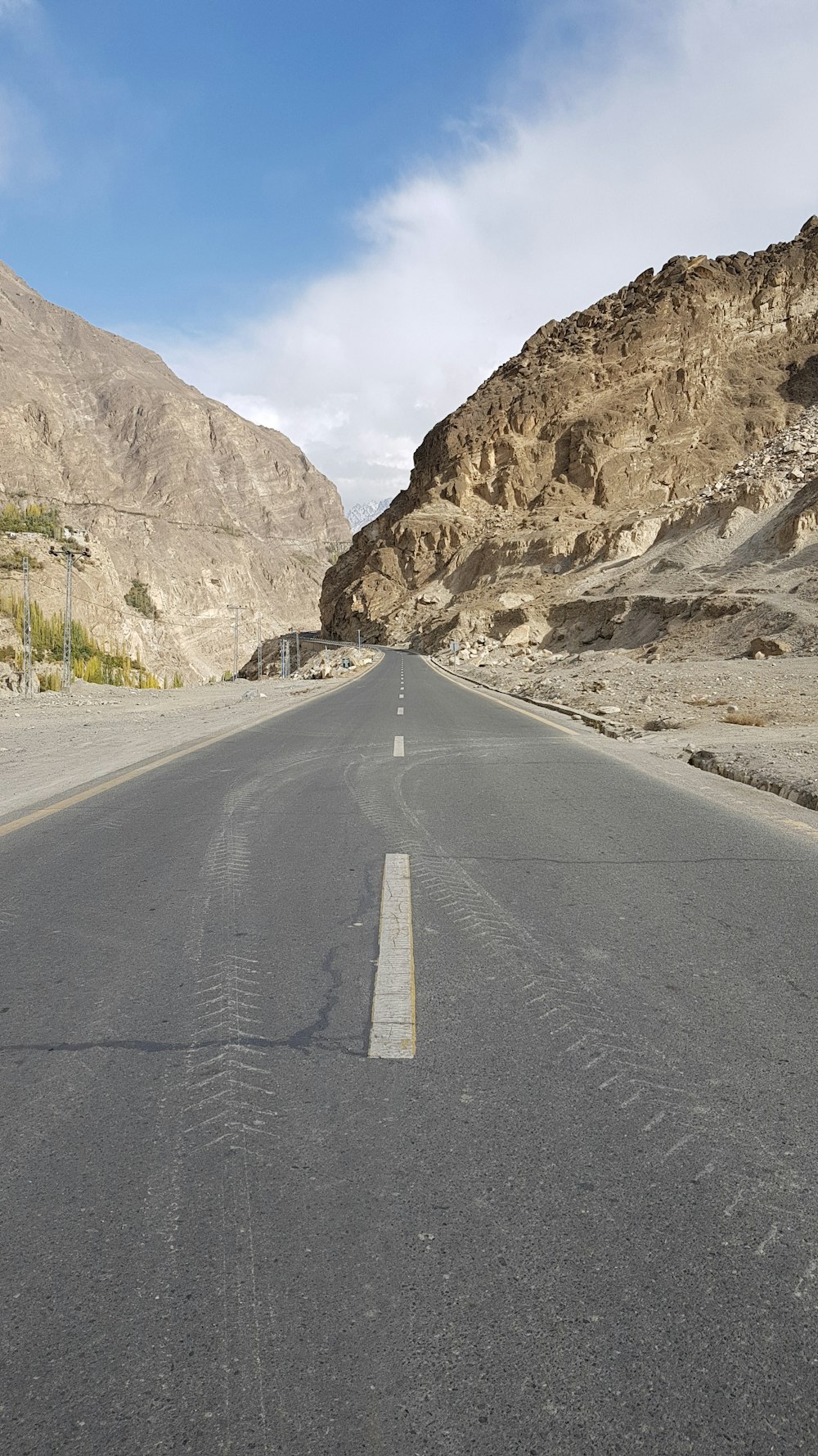 gray concrete road near brown rocky mountain under white sky during daytime