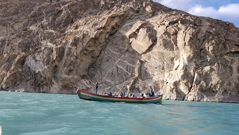 blue and red boat on body of water near brown rock formation during daytime