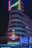 A nighttime cityscape featuring an illuminated metro sign labeled 'Callao' in front of a large building with a vibrant neon advertisement for 'Schweppes'. The background displays a classic architectural design with soft lighting and curved lines.