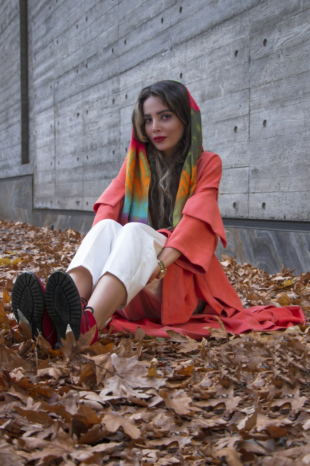 woman in green scarf and white dress sitting on dried leaves
