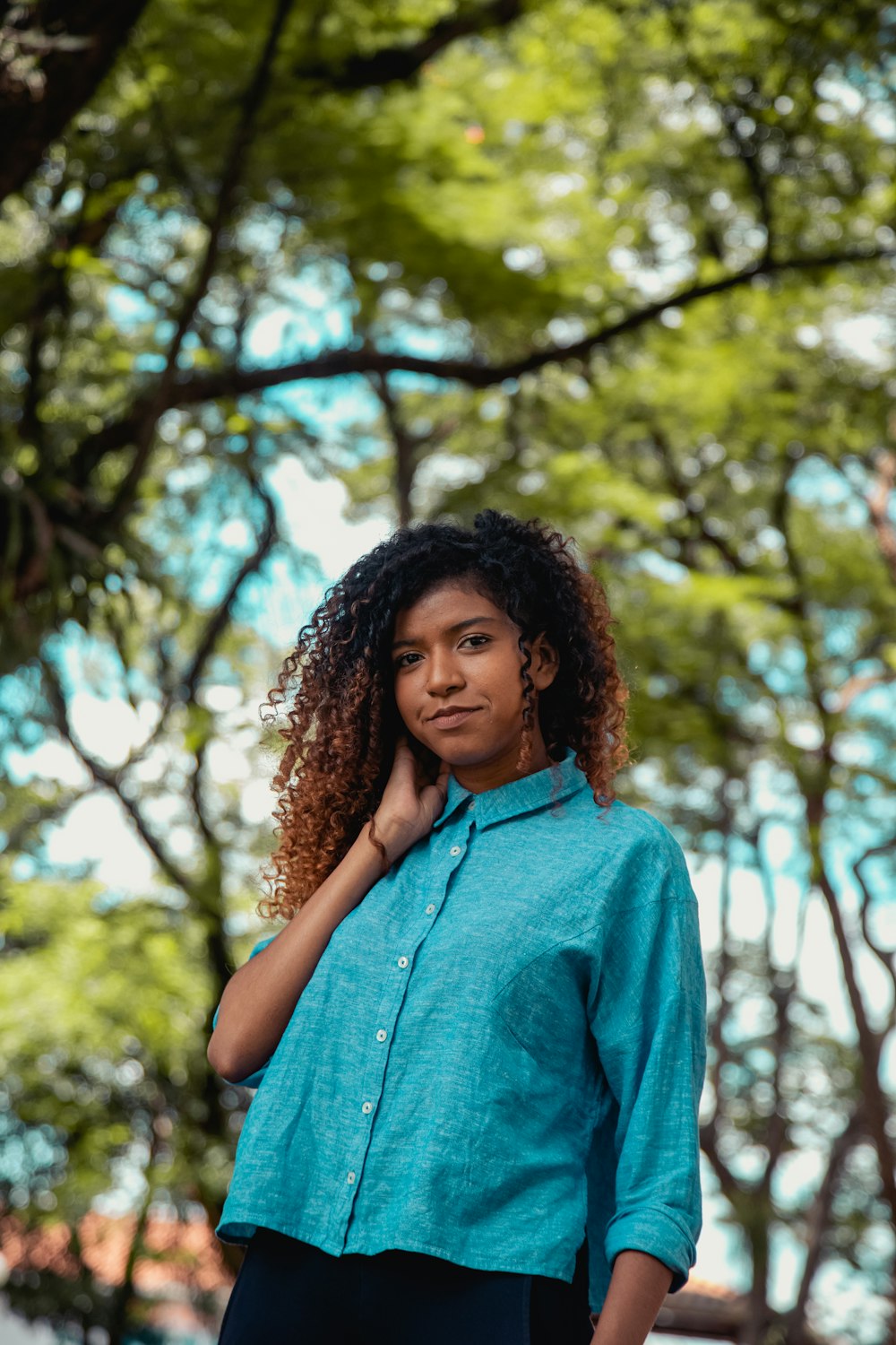 mulher no botão azul para cima camisa de pé perto da árvore marrom durante o dia