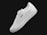 A single white sneaker with a sleek design, featuring subtle perforations along the side for ventilation. The sneaker has a classic lace-up style and branding visible on the side and heel. It is positioned at an angle against a plain black background.