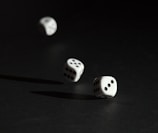 Three white dice are captured in mid-air against a dark background. The light casts shadows on the surface, highlighting the dots on each die.