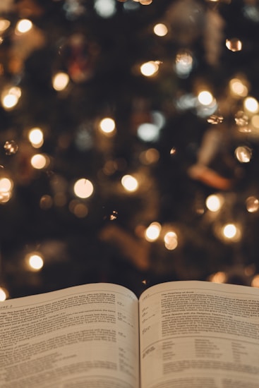 An open book with visible text in focus, set against a blurred background filled with warm, glowing lights resembling bokeh. The atmosphere is cozy and inviting.