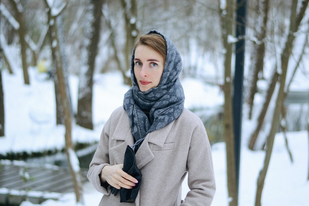 woman in gray coat and gray scarf standing on snow covered ground during daytime