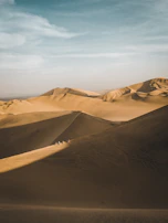 Golden sand dunes stretching endlessly in the desert at sunset, with a lone camel caravan crossing the horizon.