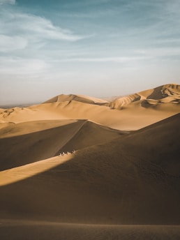 A sunlit Moroccan desert caravan winding through golden dunes under a vast sky.