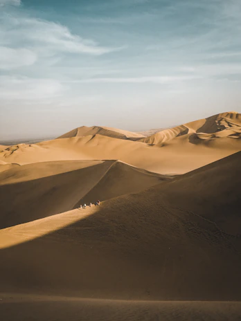 Travelers riding camels across golden dunes under a clear blue sky.