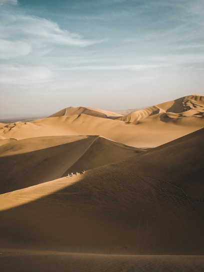 A golden camel caravan winding through towering sand dunes under a vibrant sunset sky.