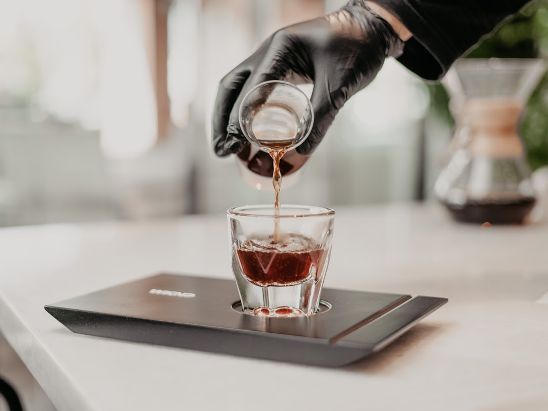 person pouring brown liquid on clear drinking glass