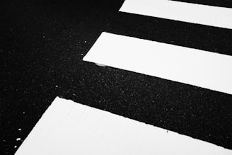 A close-up view of a pedestrian crosswalk, displaying the contrast between the white painted stripes and the dark asphalt road.