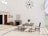 A modern dining room with minimalist decor features a sleek table and chairs on a large patterned rug. A potted plant sits centered on the table. The room is well-lit with large windows allowing natural light to enter. A stylish chandelier hangs from the ceiling. A stone fireplace, small console table, and decorative wall art complete the design.